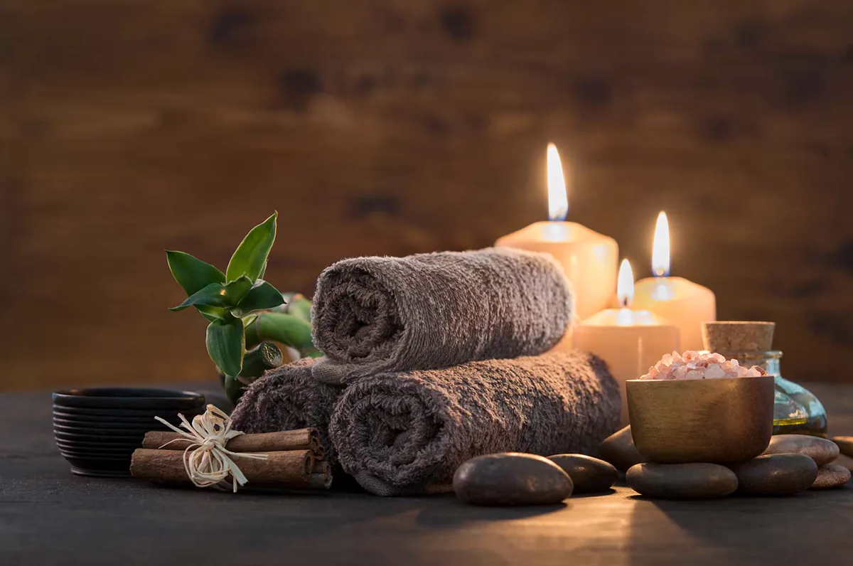 Gerollte Handtücher und brennende Kerzen für eine Wellness-Auszeit